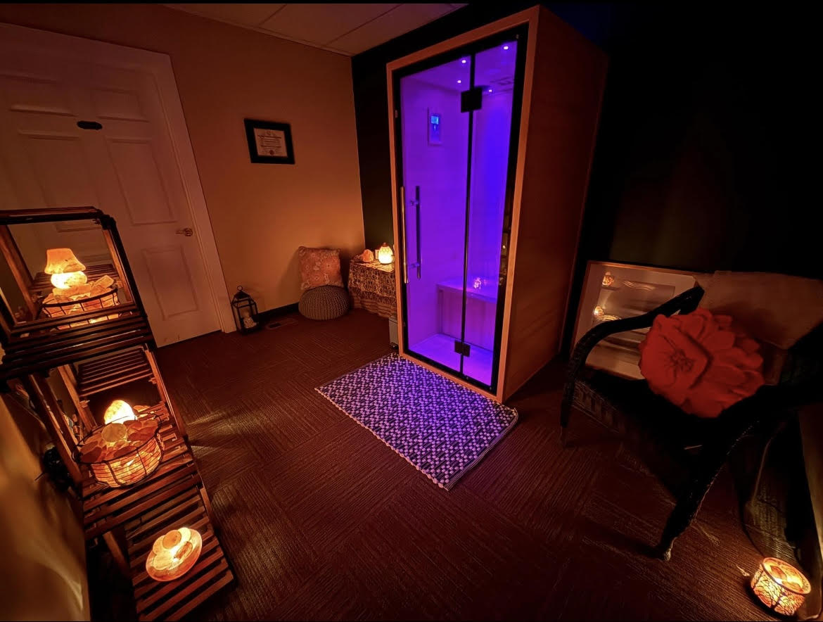 Infrared sauna with purple light inside a room with candles and a chair.